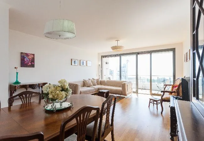 A bright living and dining area has a large table and seating beside wide windows.