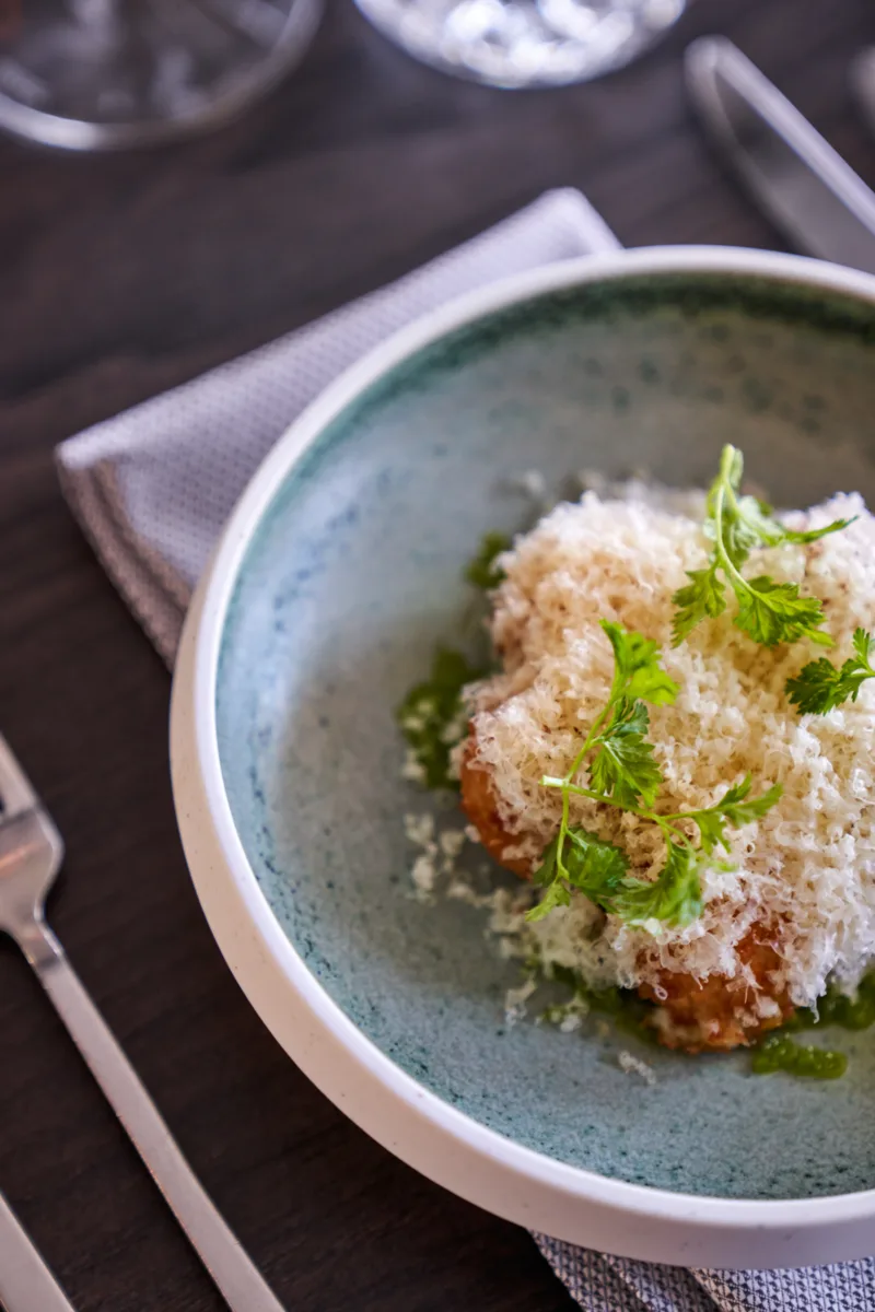Representative hotel space: A plated dish topped with grated cheese and fresh herbs on a dark table.