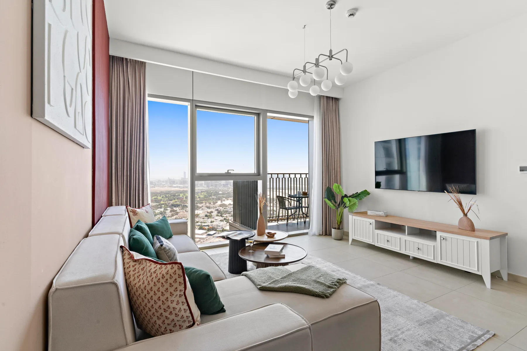 A bright living room with seating, a television, and large windows opening onto a balcony.