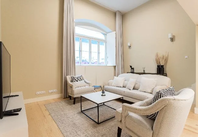 A bright living room with light seating, a coffee table, and a large window.
