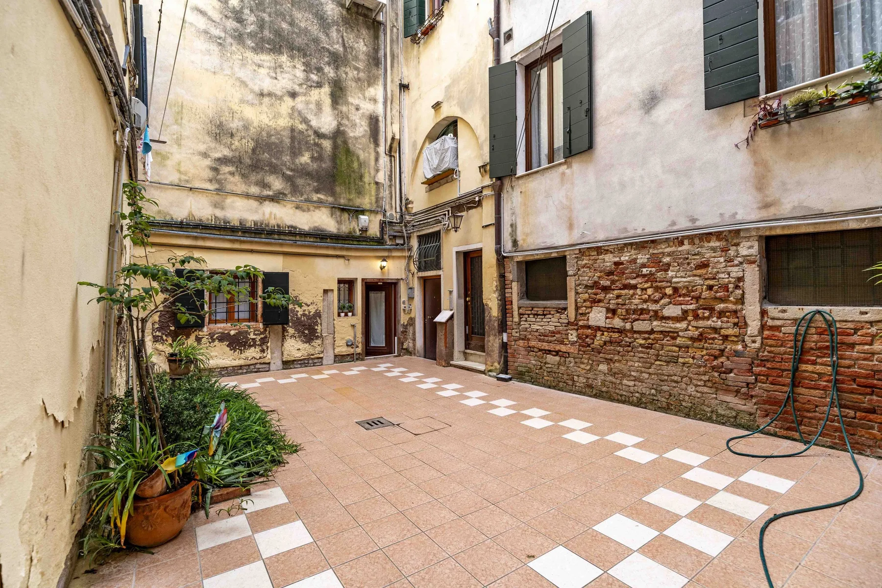 Zona común: Un patio cerrado con suelo de baldosas, plantas y fachadas de edificios alrededor.