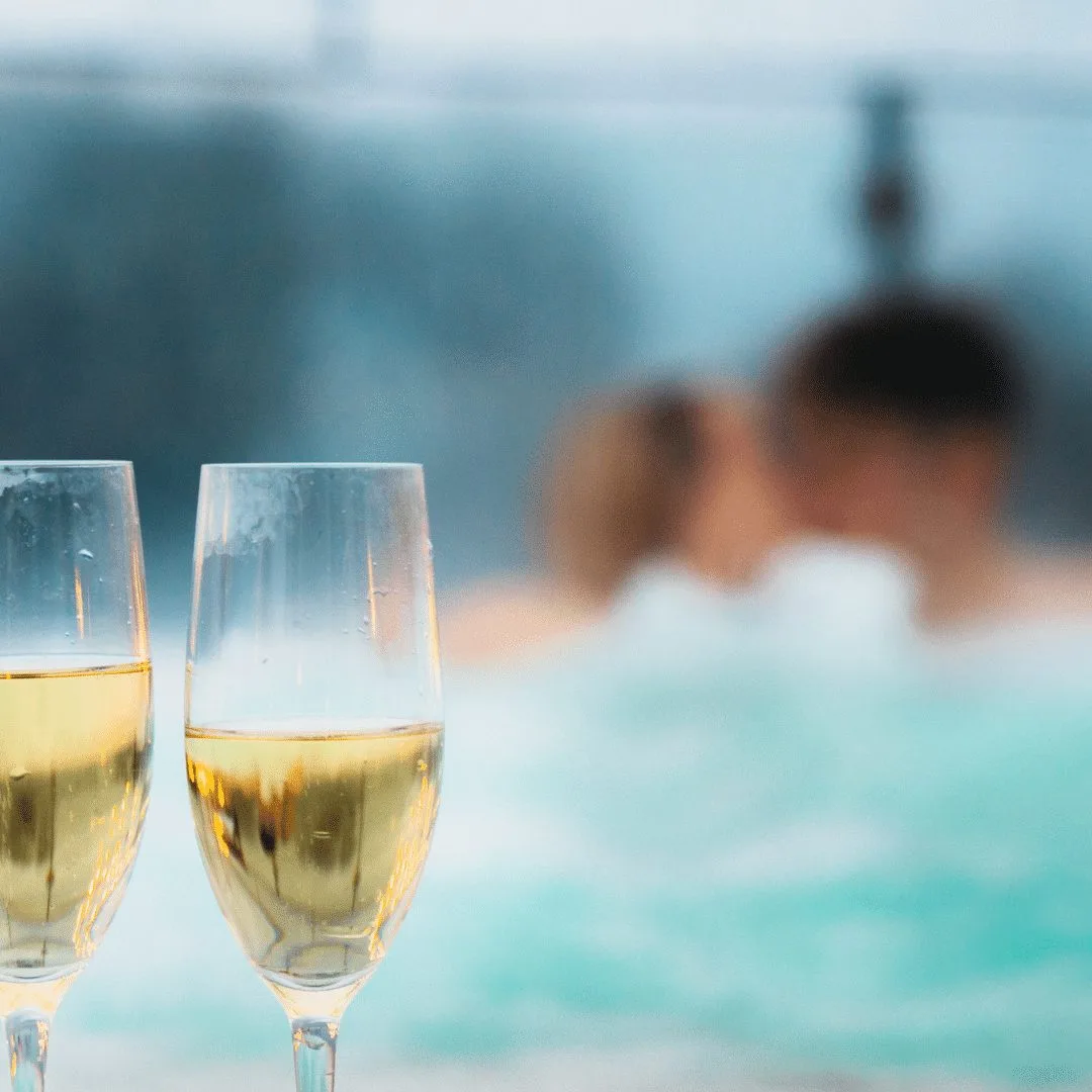 Espacio representativo del hotel: Dos copas de vino espumoso junto a una piscina, con personas nadando desenfocadas al fondo.