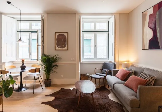 Una sala luminosa con sofá, zona de estar y ventanas grandes.