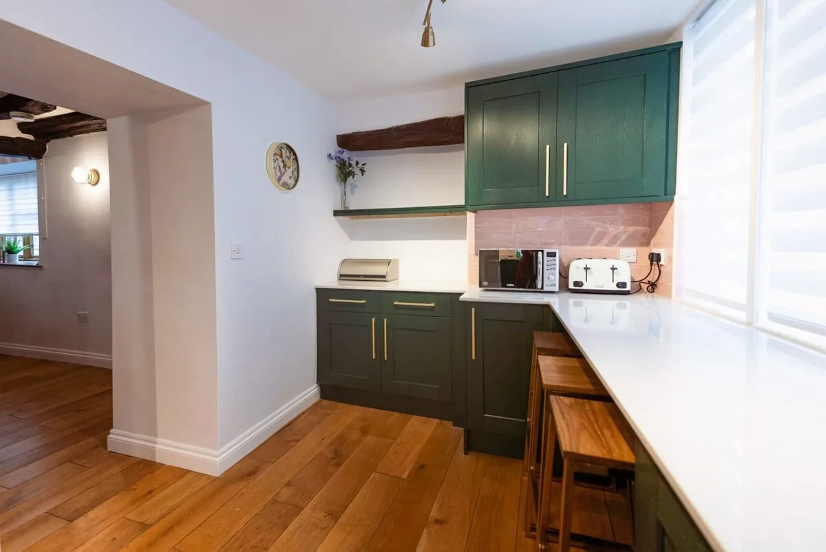 Una cocina compacta con gabinetes verde oscuro y una encimera blanca larga.