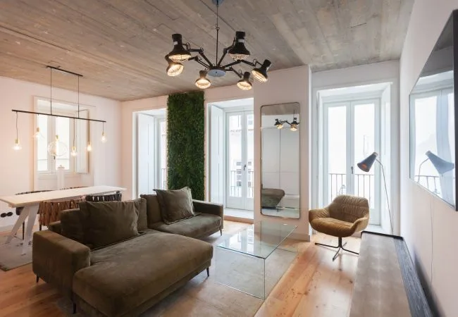 A bright living room with seating, a glass coffee table, and tall windows.