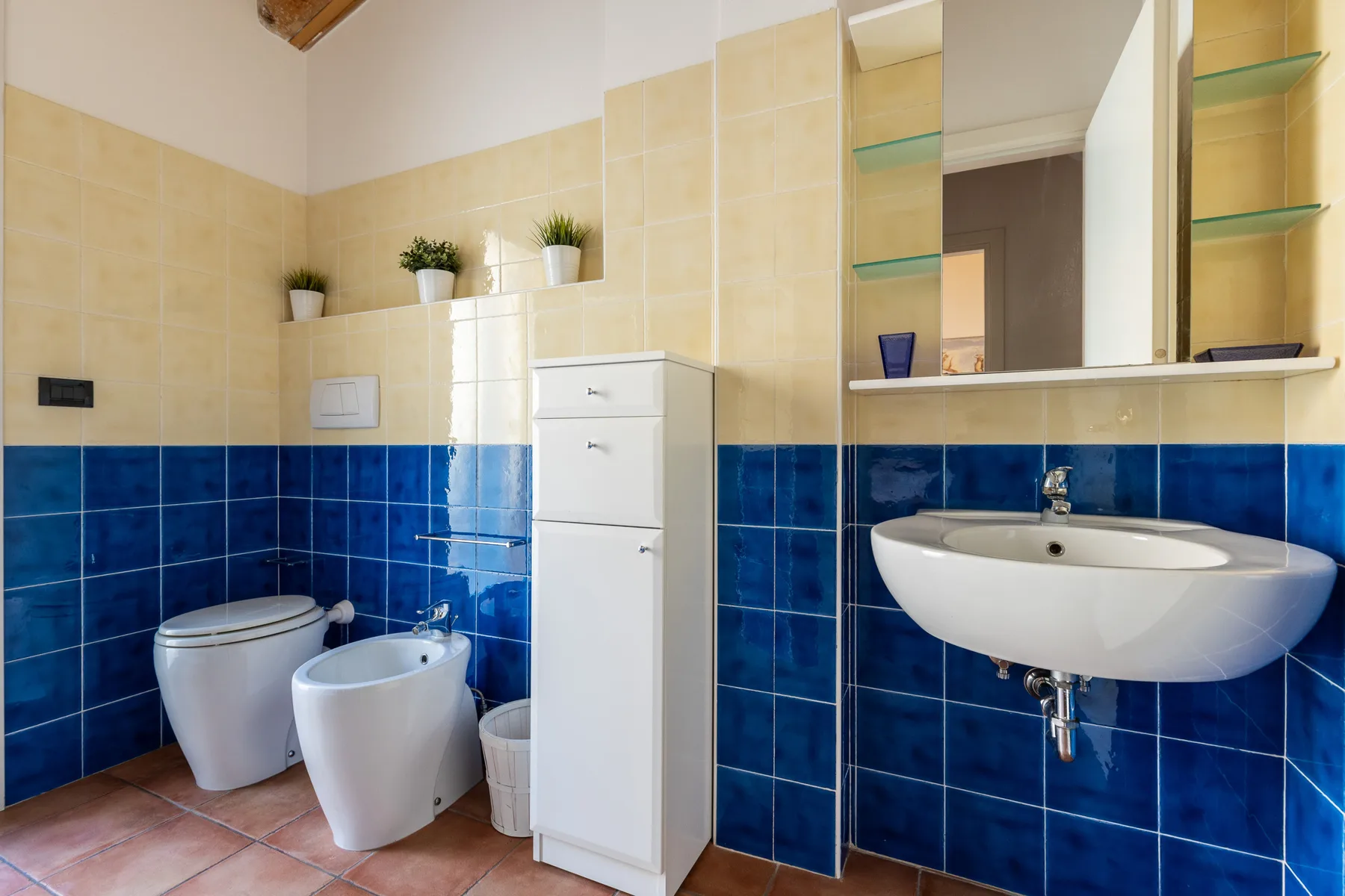 Un baño alicatado con inodoro, bidé, lavabo y armario blanco.