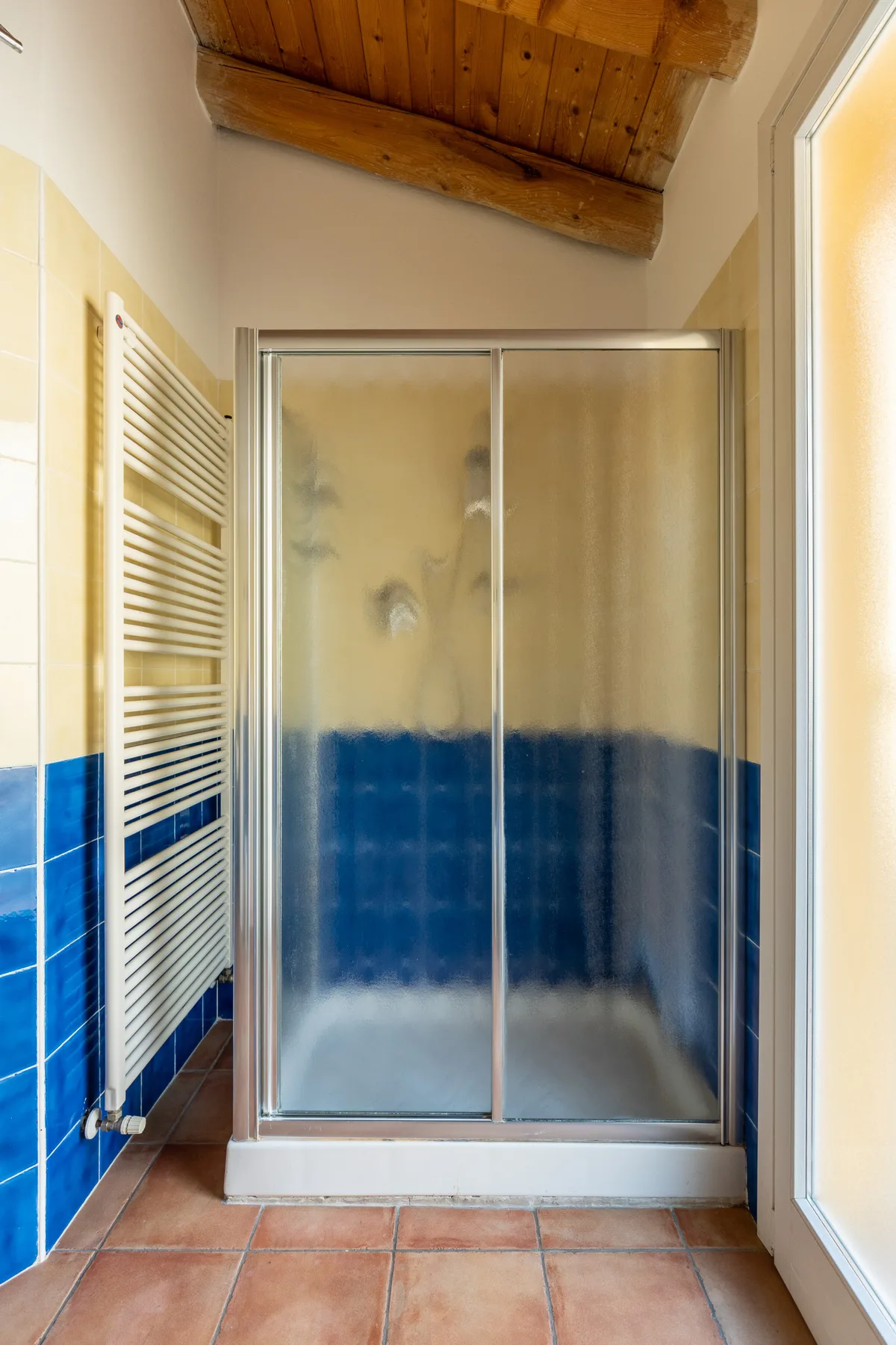 Un baño con una ducha de cristal y paredes de azulejos azules.