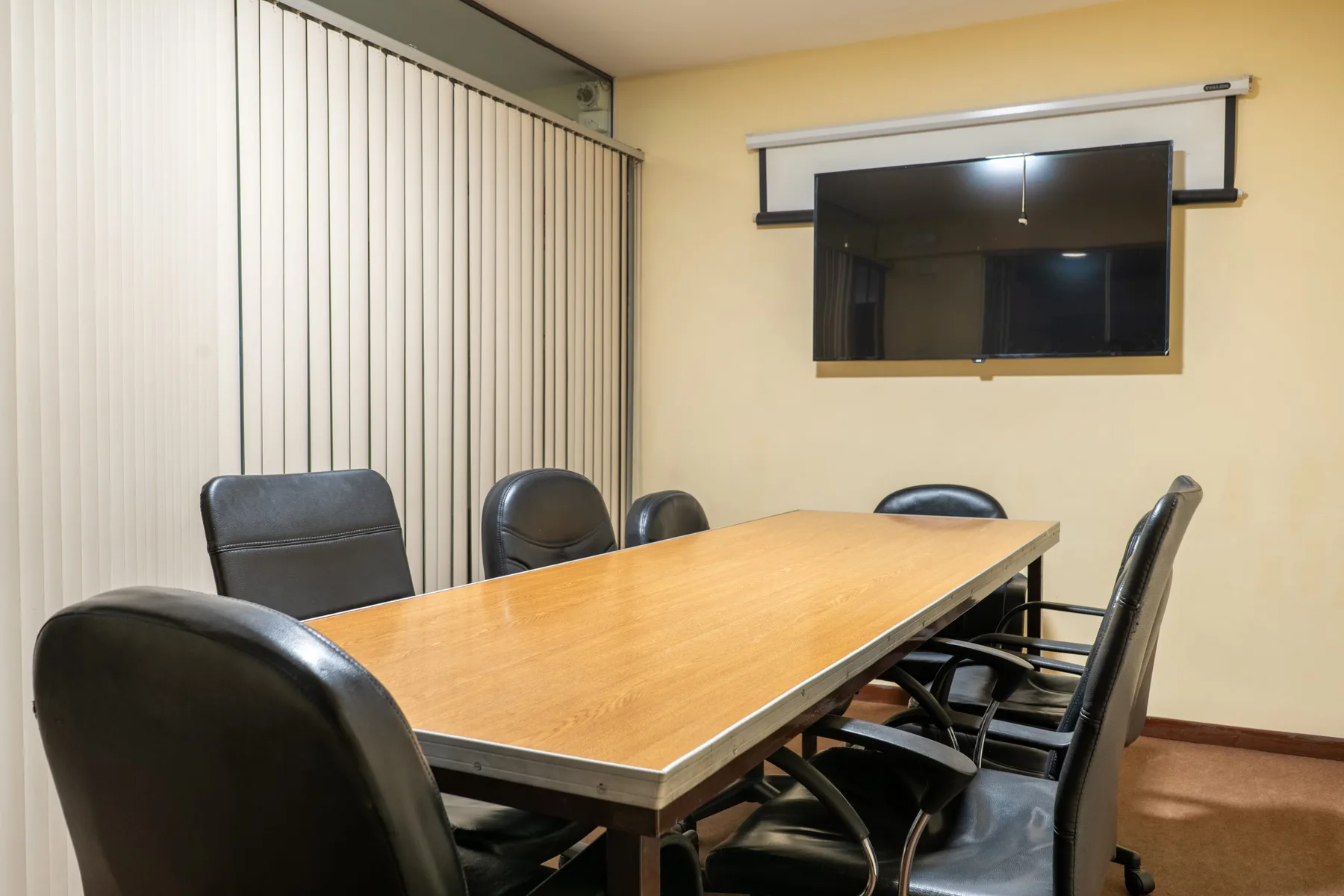 Espacio representativo del hotel: Una sala de reuniones con una mesa larga, asientos y una pantalla en la pared.