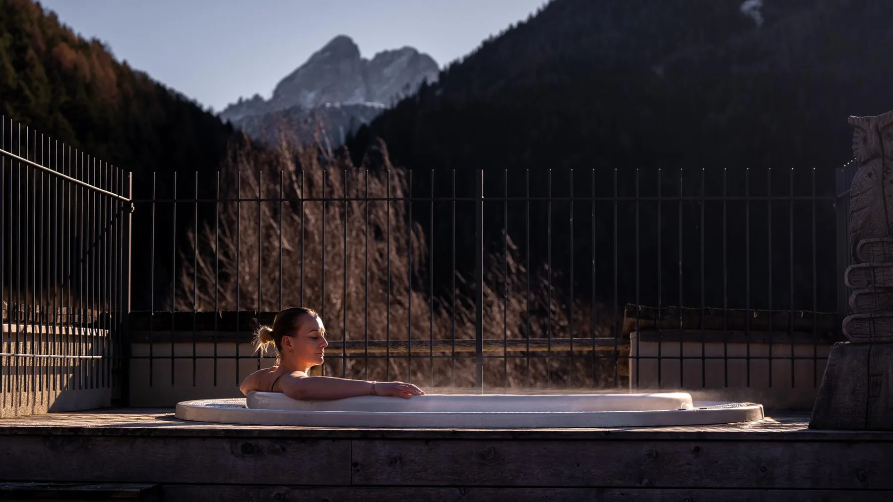 Espacio representativo del hotel: Una bañera de hidromasaje al aire libre está en una terraza con montañas al fondo.