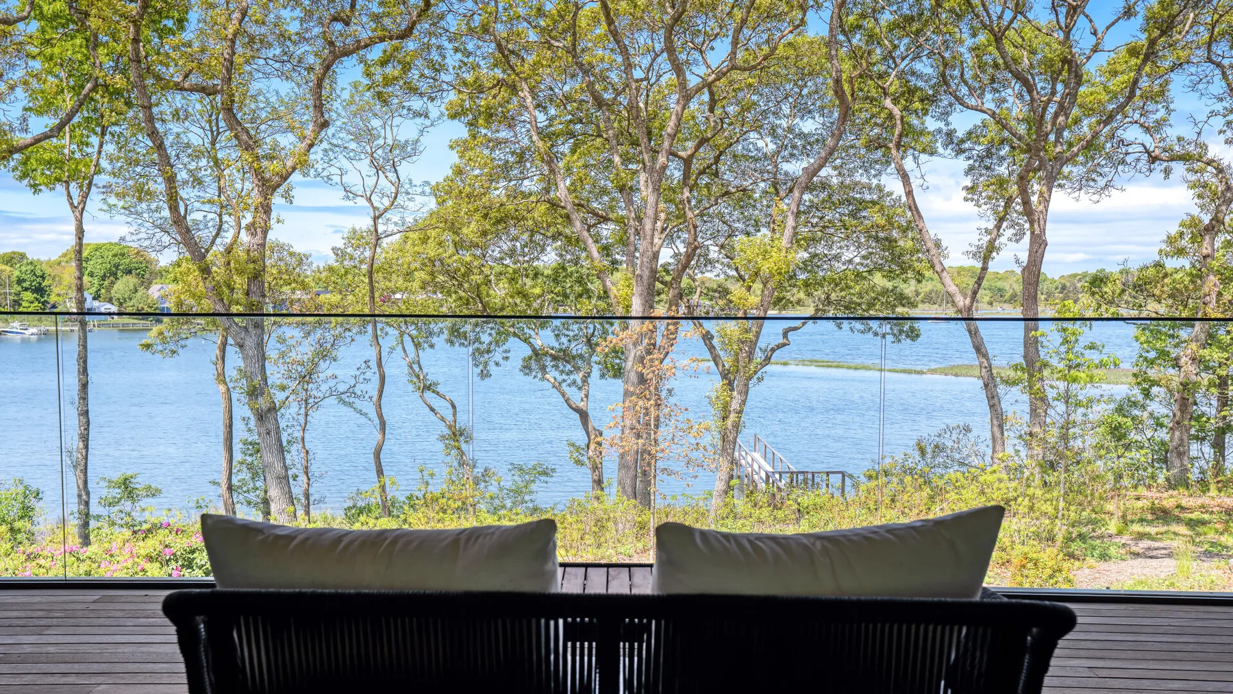 A lakeside seating area faces the water through a glass railing.