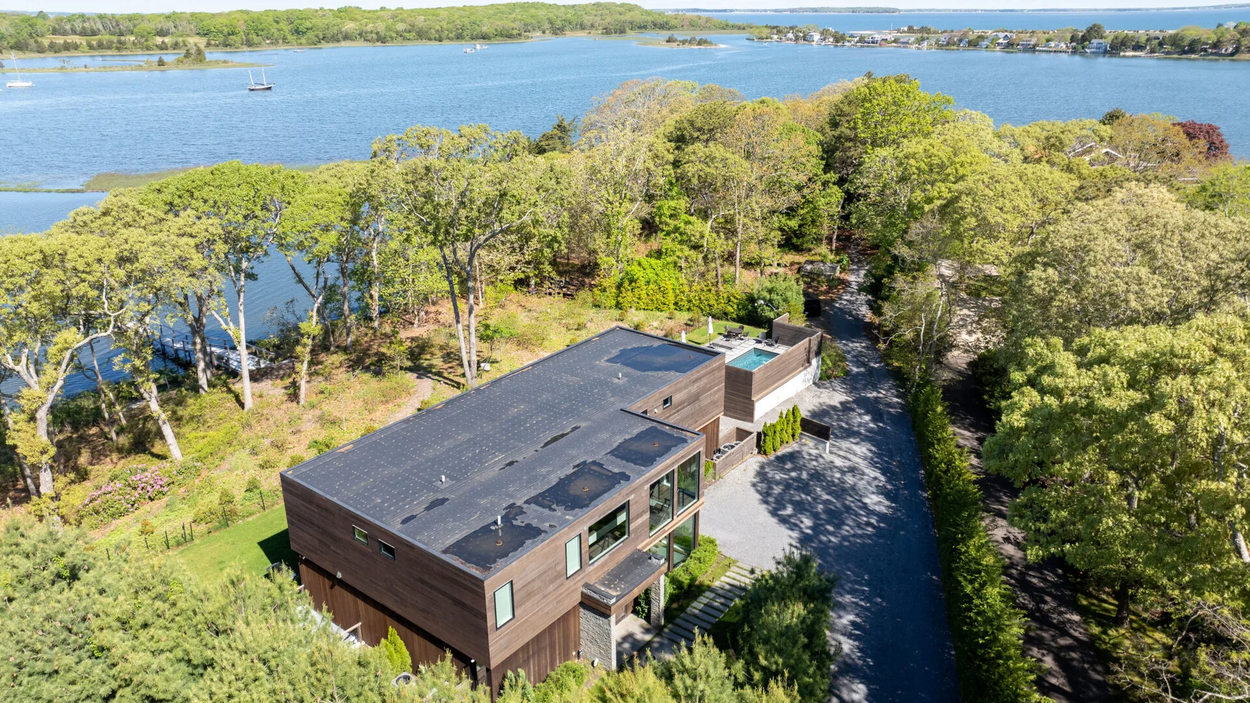 A modern house sits among trees beside a broad waterfront.