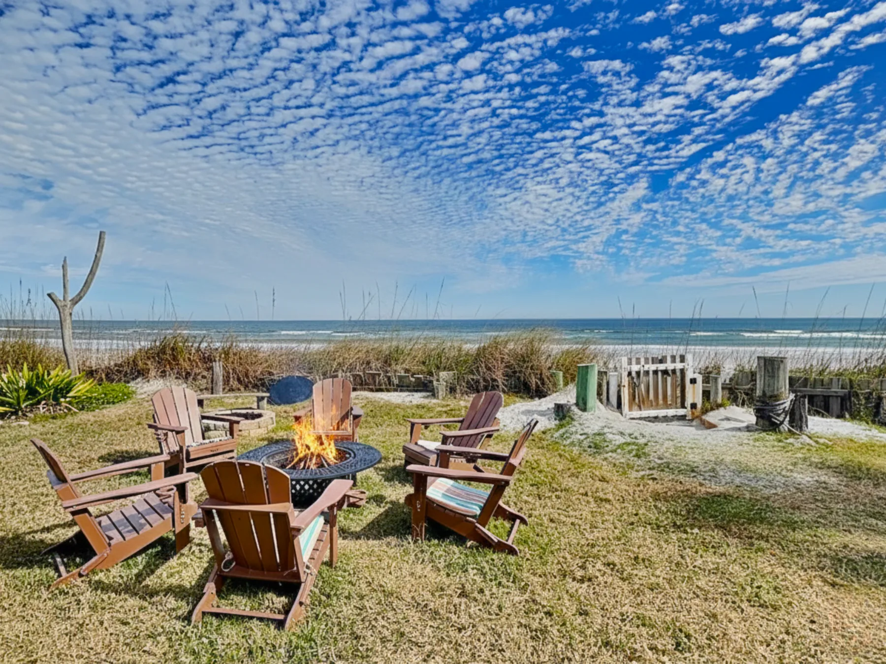 Outdoor seating surrounds a fire pit on a grassy lawn beside the beach.