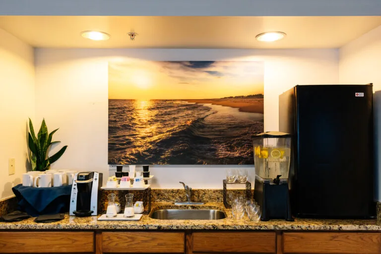 Representative hotel space: A refreshment counter with a sink, beverage dispensers, and a large beach sunset image.