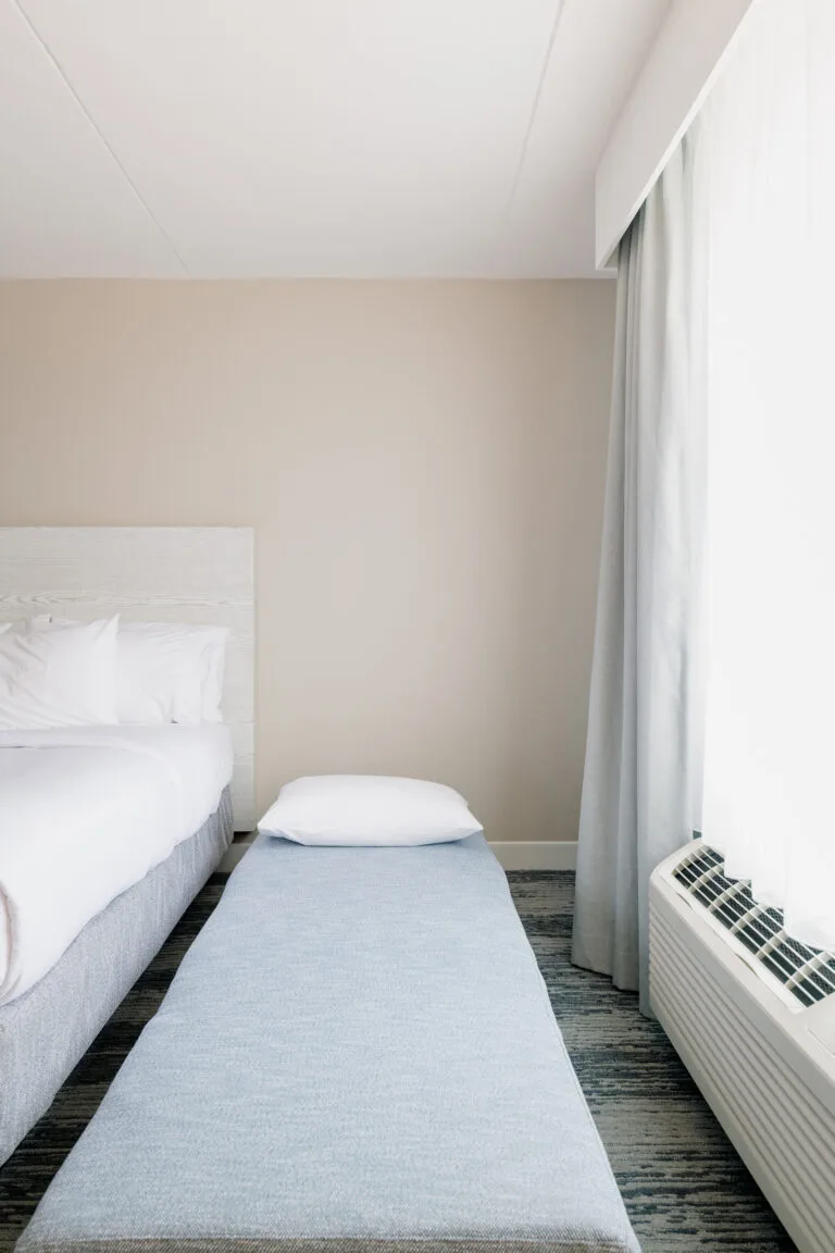Representative hotel space: A bedroom with a bed and a narrow upholstered bench beside the window.