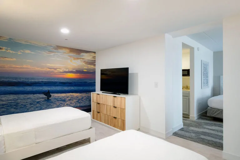 Representative hotel space: A bedroom with two beds, a television, and a large ocean sunset mural.