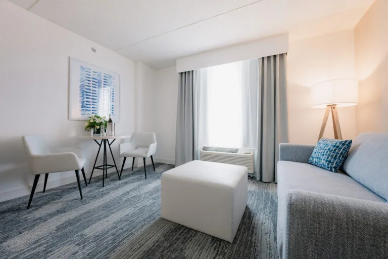 Representative hotel space: A bright living room with seating, a coffee table, and large curtained windows.