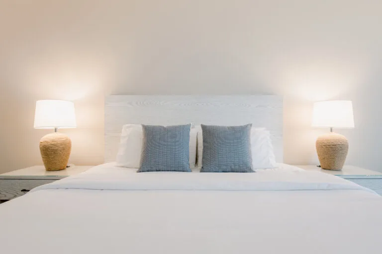 Representative hotel space: A neatly made bed with blue pillows and matching bedside lamps.