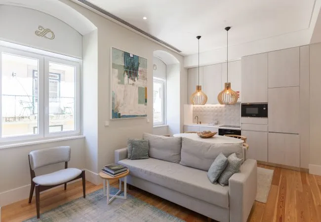 A bright living room with a gray sofa and an open kitchen.
