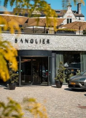 Representative hotel space: Hotel entrance beneath a stone sign, with patio umbrellas above.