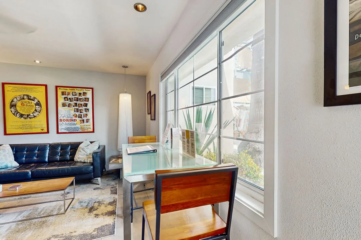 A bright living and dining area has a glass table beside large windows.