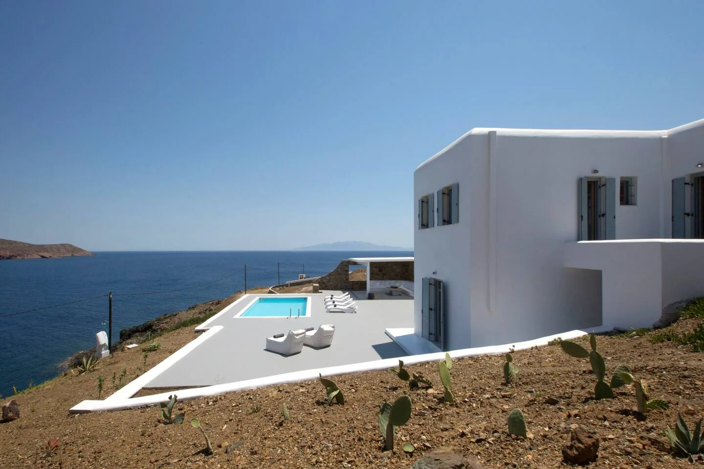 A white modern house overlooks the sea, with a swimming pool on the terrace.