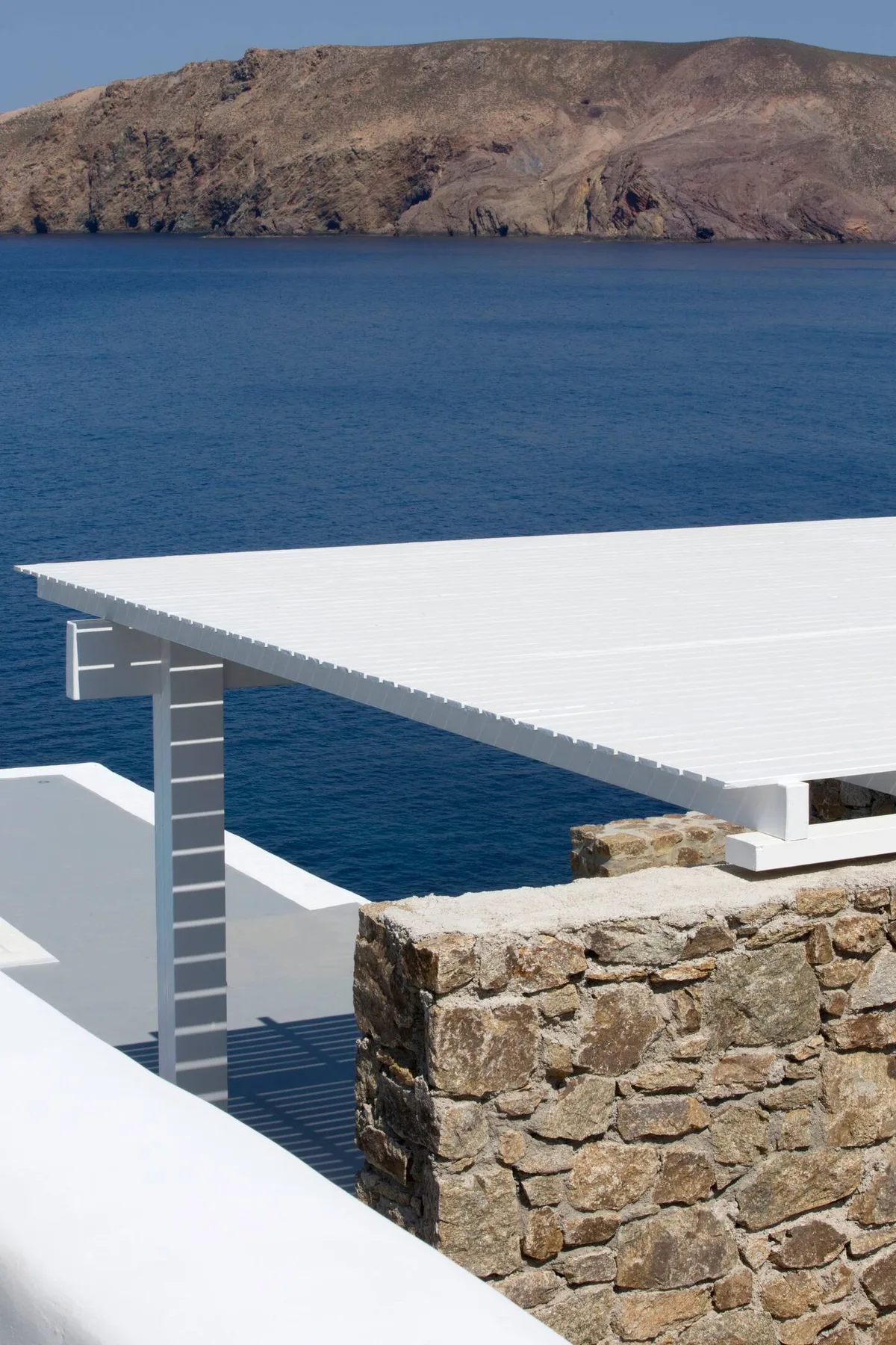 A white terrace overlooks blue water and a rocky shoreline.