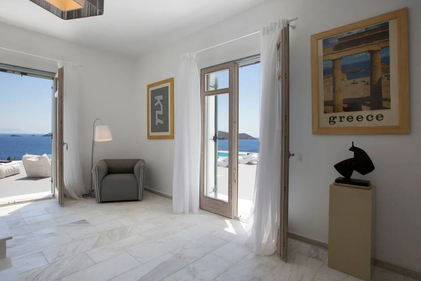 A bright room opens onto a sea-view terrace, with a lounge chair beside the windows.