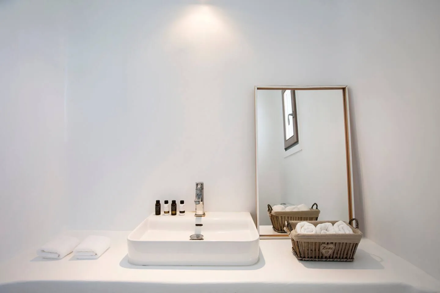 A bathroom vanity with a sink, mirror, and baskets of folded towels.