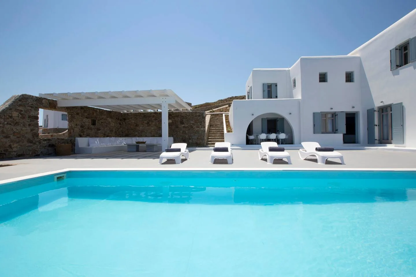 A swimming pool in front of a white building, with lounge seating along the edge.
