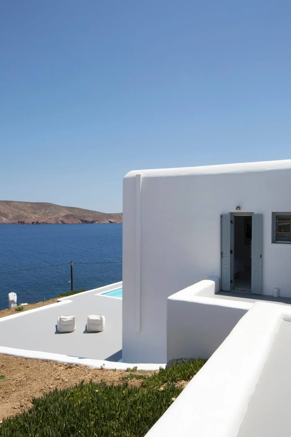 A white seaside building overlooks blue water and a small terrace.