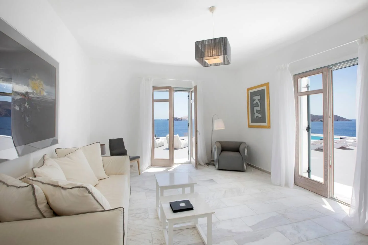 A bright living room with seating and open doors facing the sea.