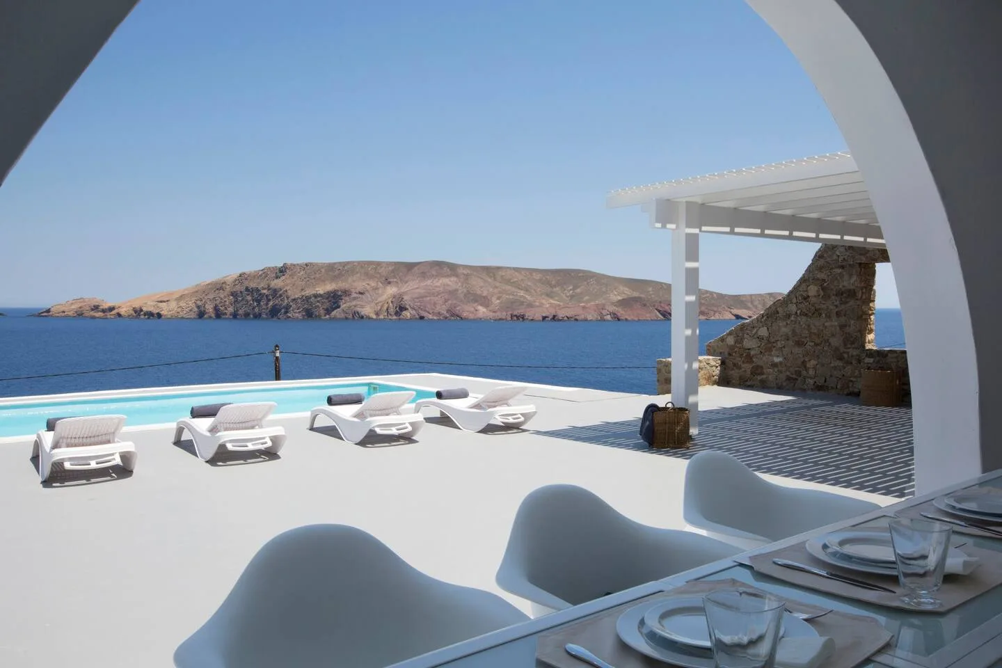 A seaside terrace with lounge seating, a shaded dining area, and views across the water.