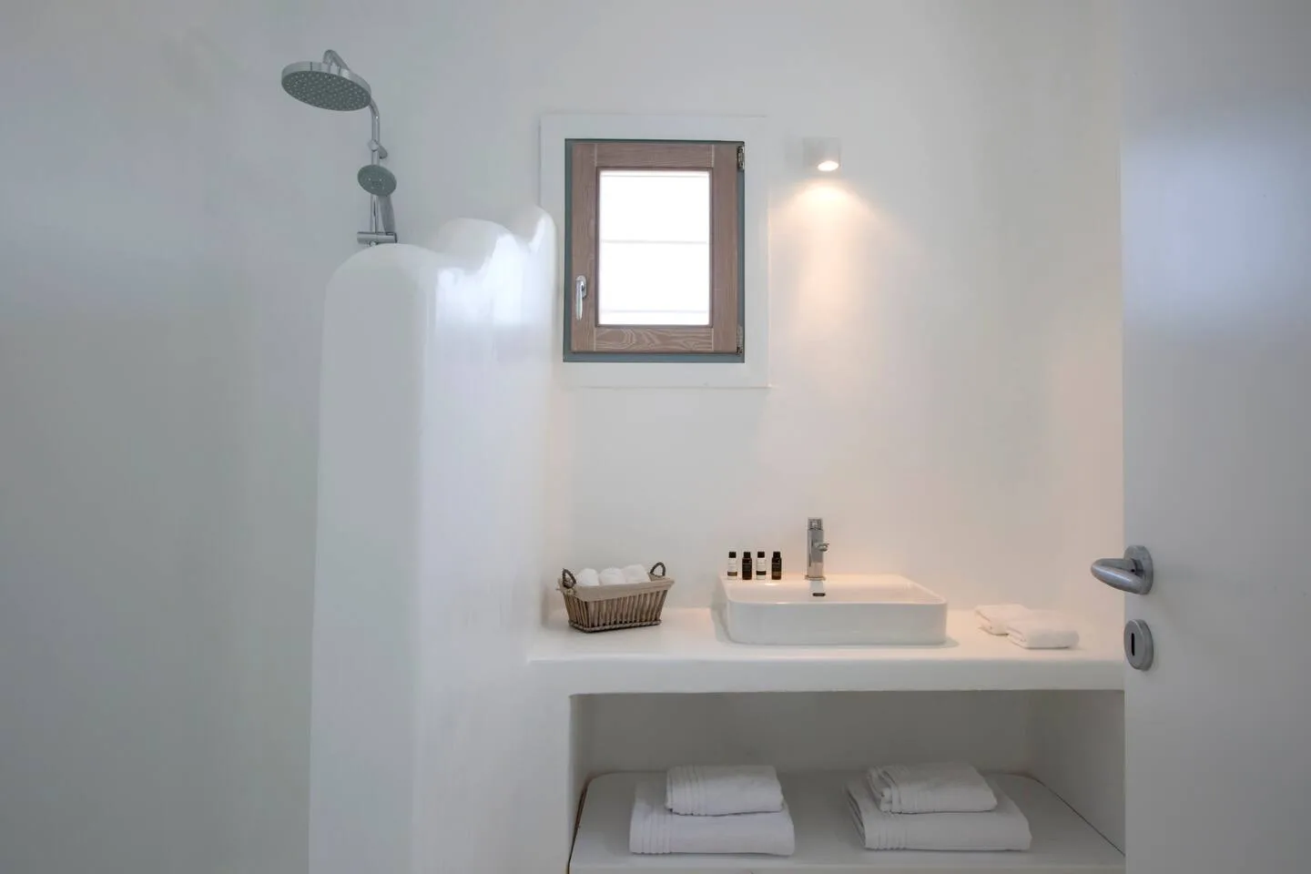 A bright bathroom with a shower, a sink, and a small window.