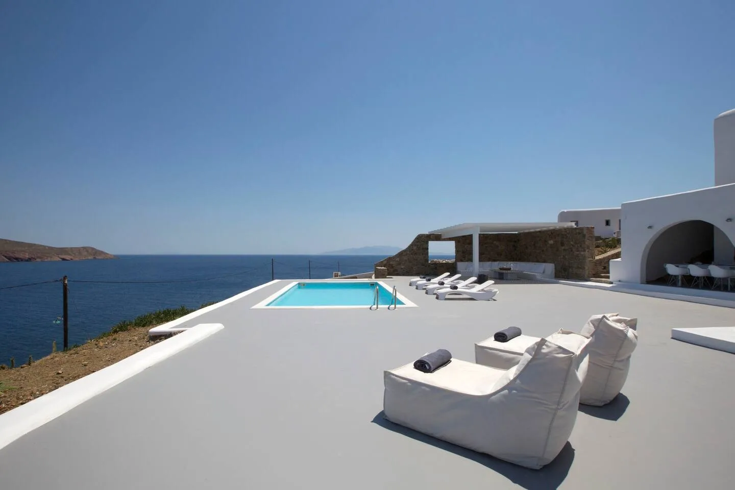 A seaside terrace with a swimming pool and cushioned lounge seating.