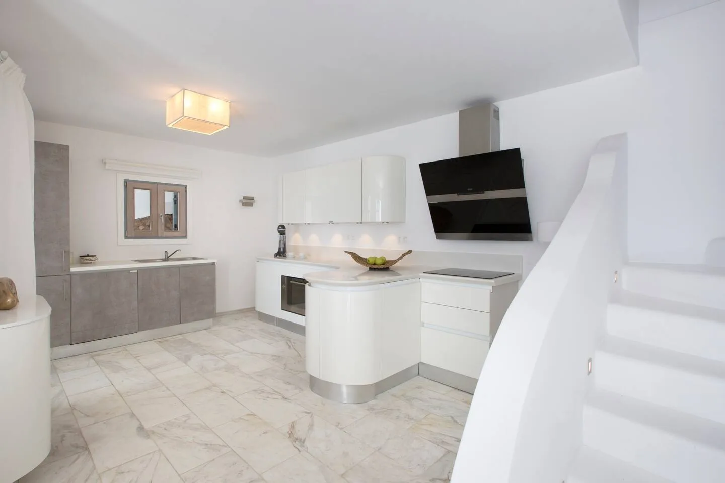 A bright modern kitchen with white cabinets, a central island, and a dark range hood.