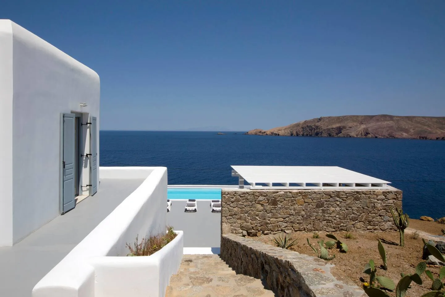 A white seaside building overlooks the blue water and a rocky coast.