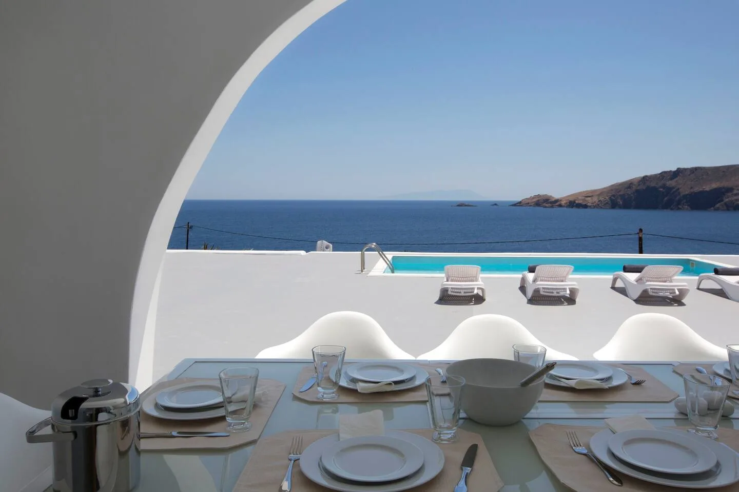 A dining table overlooks a pool and the sea through a curved opening.