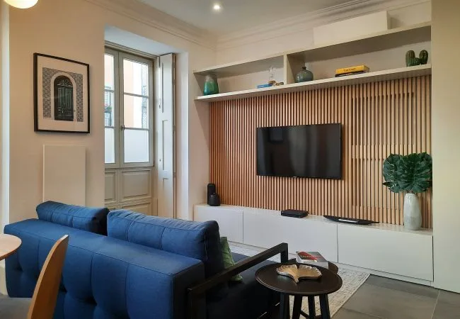 Una sala de estar con asientos azules frente a un televisor en la pared.