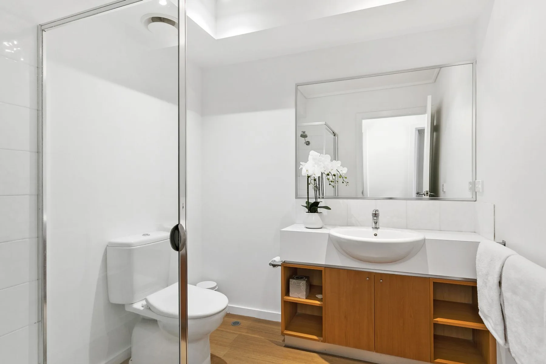 Baño luminoso con lavabo y mampara de ducha de vidrio.