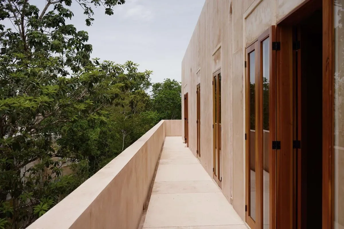 An exterior balcony walkway runs beside a building, with trees beyond the railing.