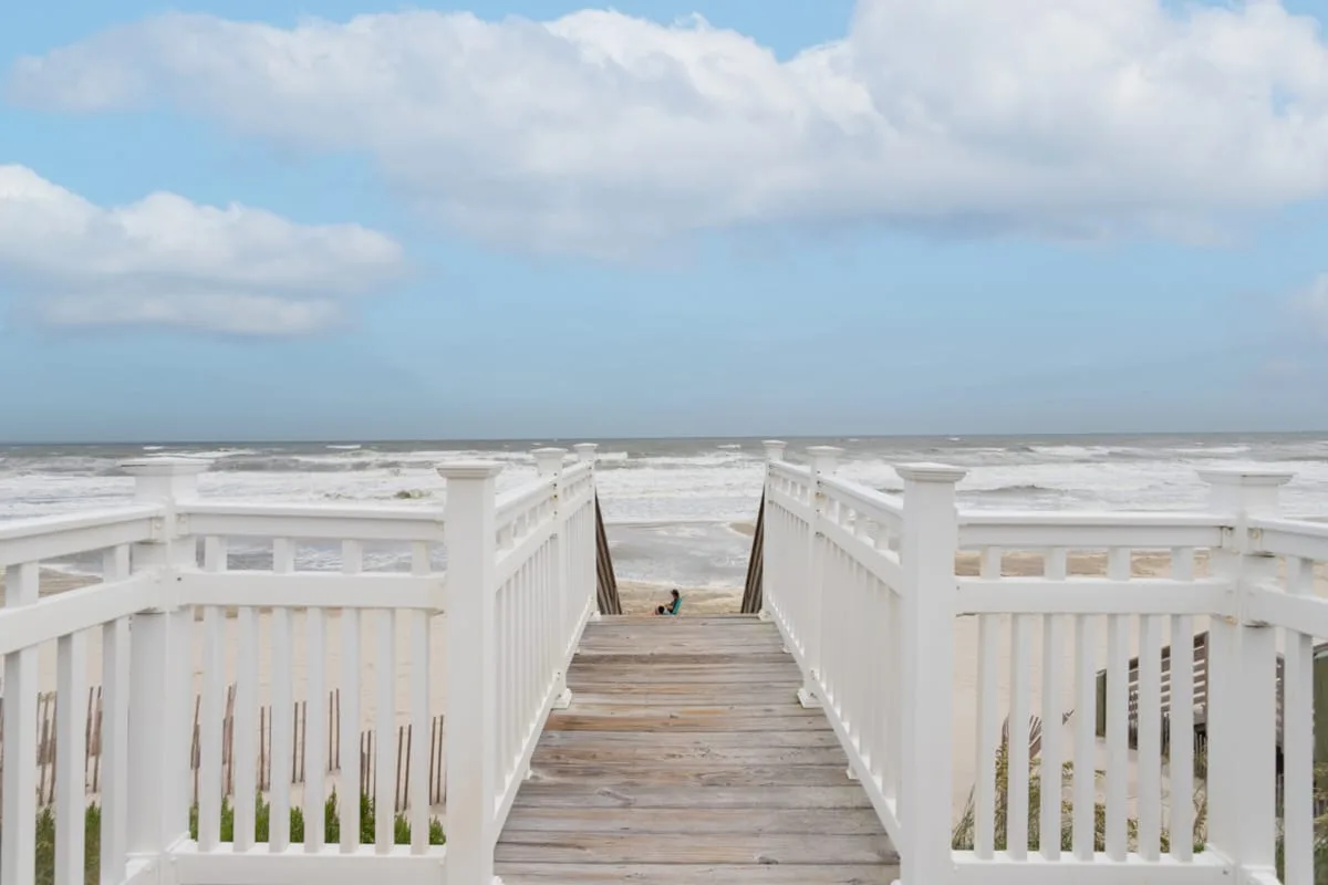 A wooden boardwalk with white railings leads toward the ocean.