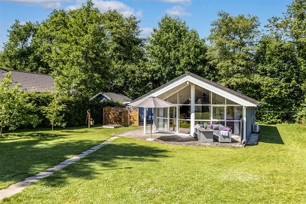 A glass-fronted house opens onto a lawn, with outdoor seating beneath a patio umbrella.