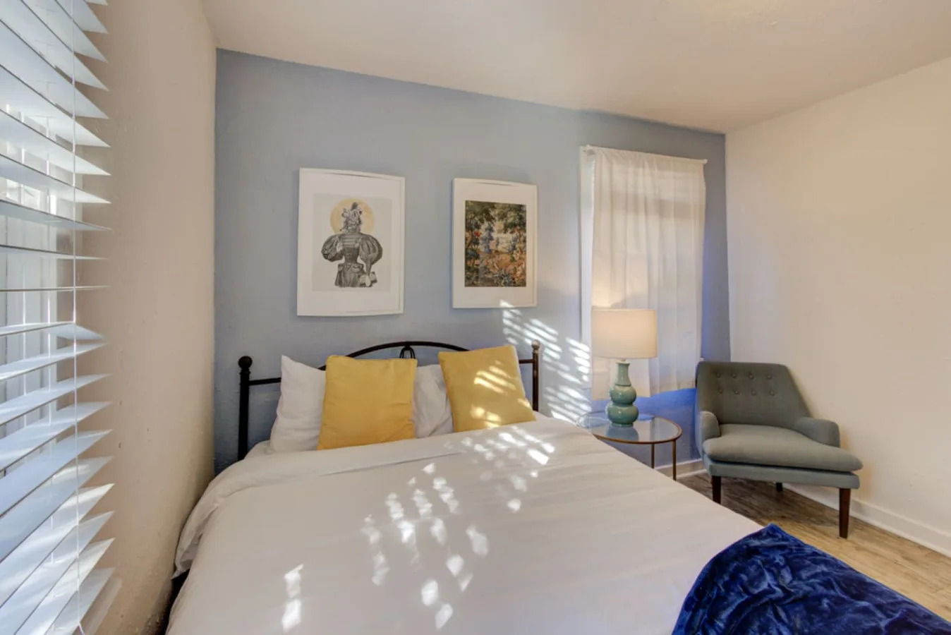 A bedroom with a bed, framed artwork, and a chair beside the window.