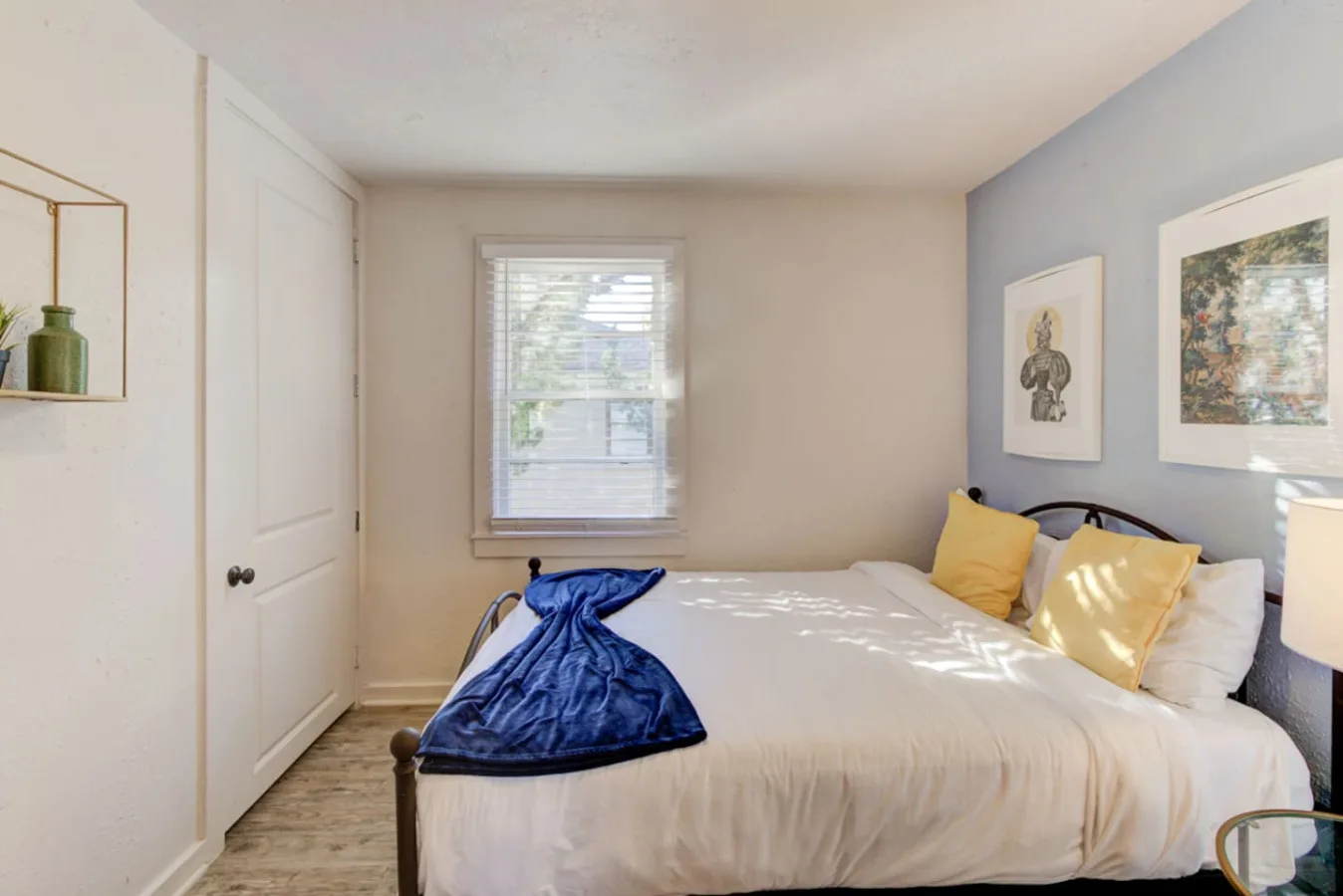 A bedroom with a bed, yellow pillows, and a window with blinds.