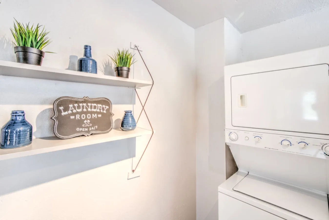 A laundry room with a front-loading washer and decorative shelves.