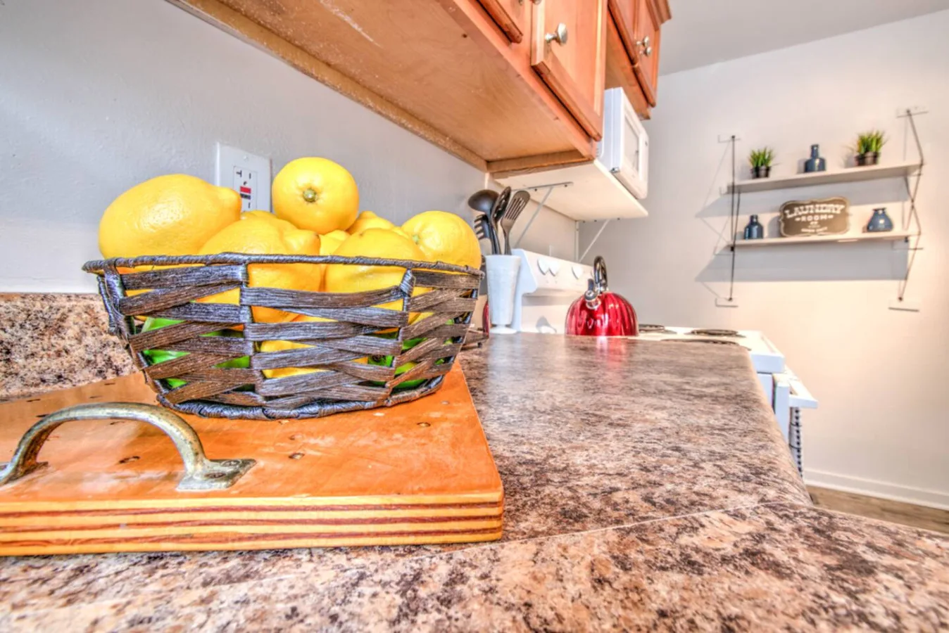 A kitchen countertop holds a basket of lemons beside a cutting board.