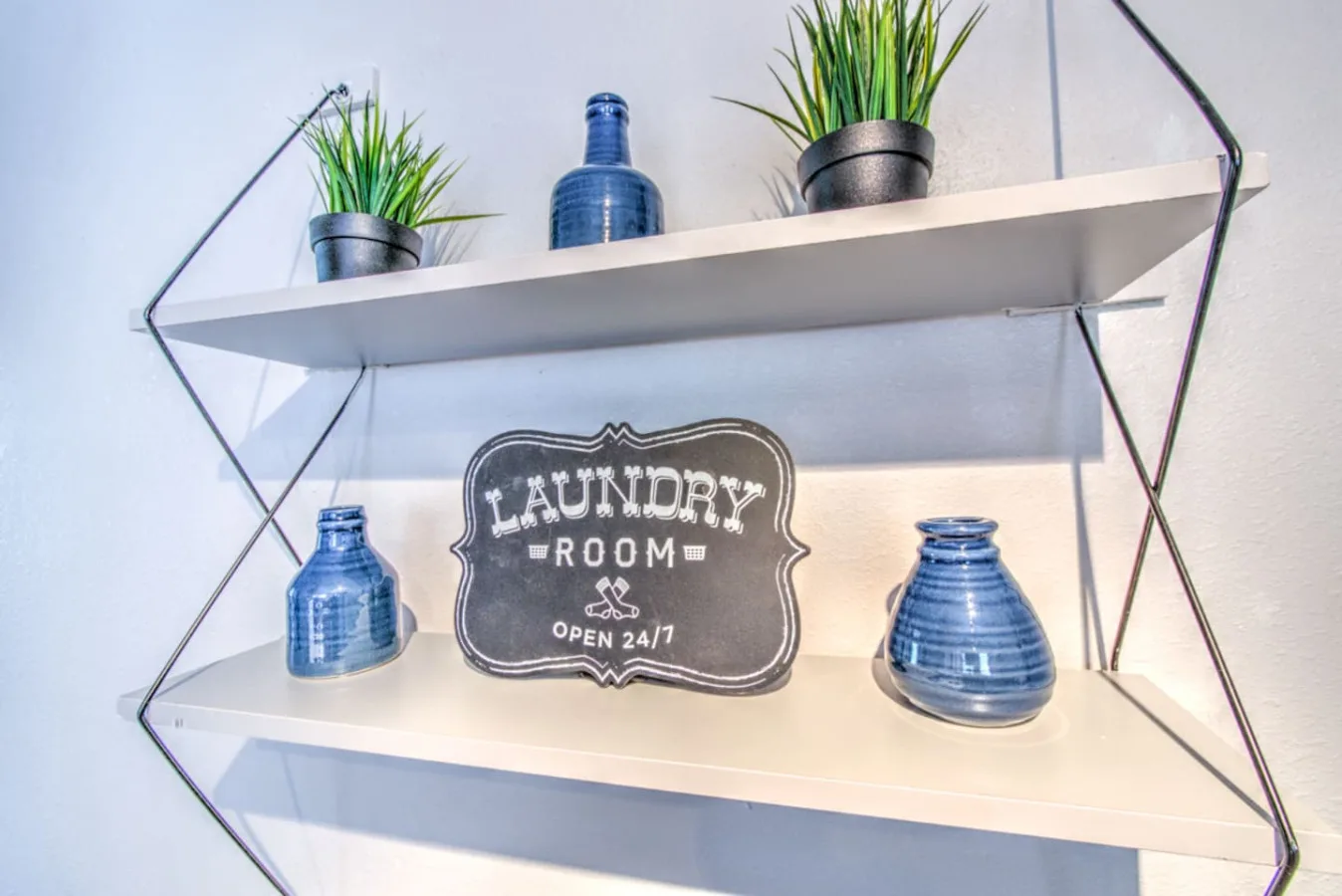 Decorative wall shelves display blue glass vases, potted plants, and a laundry room sign.
