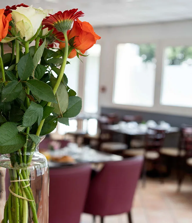 Espacio representativo del hotel: Un comedor con mesas y sillas aparece detrás de un florero con flores.