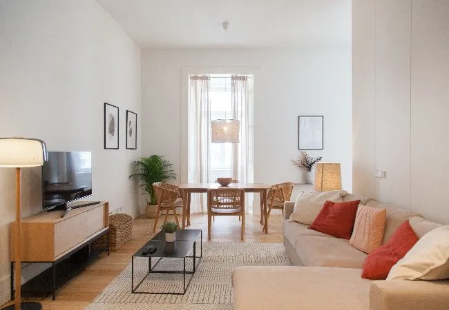 Una sala luminosa con asientos, un televisor y una mesa de comedor junto a la ventana.