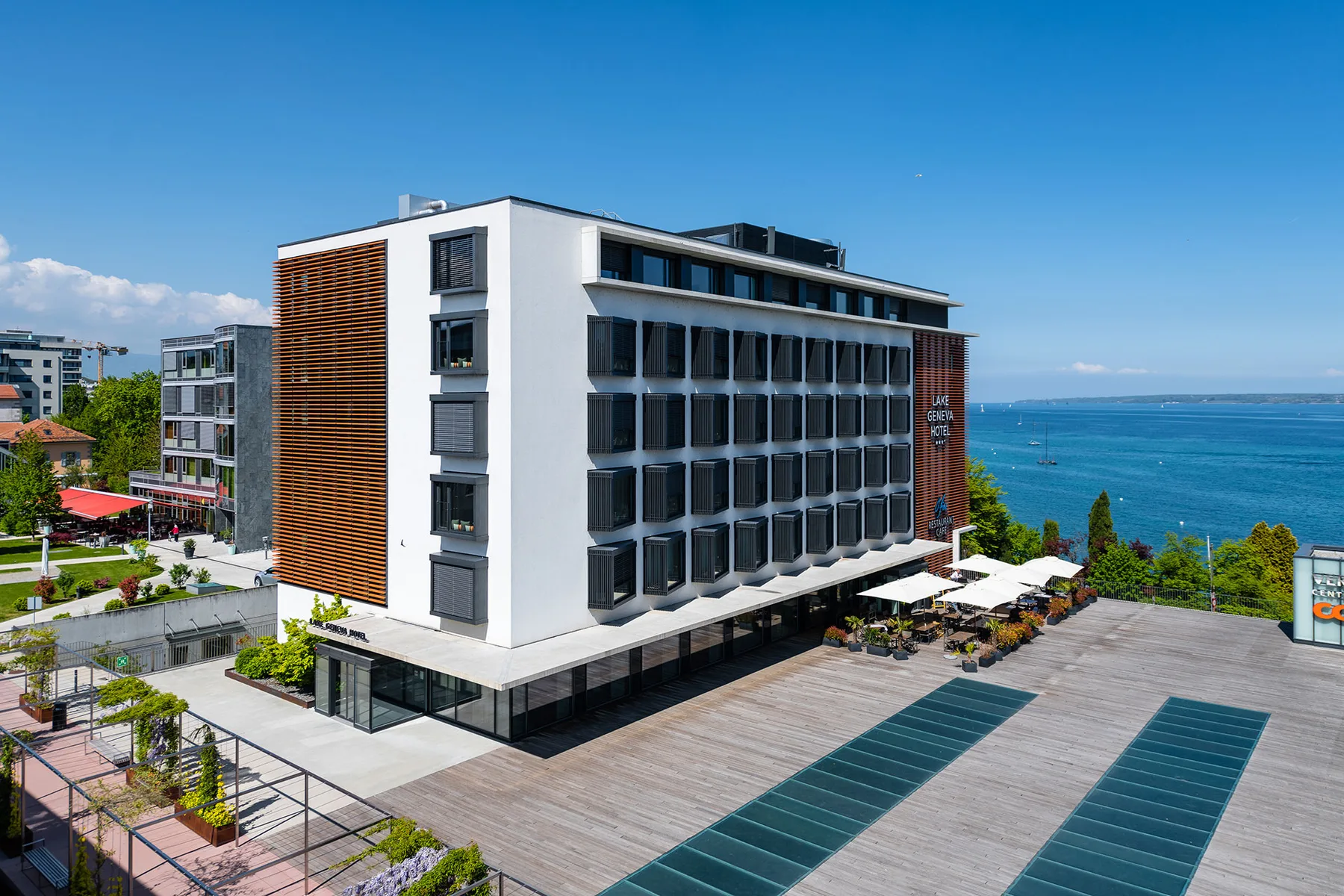 Espacio representativo del hotel: Un edificio moderno de varios pisos se alza junto al mar, con una amplia terraza pavimentada delante.